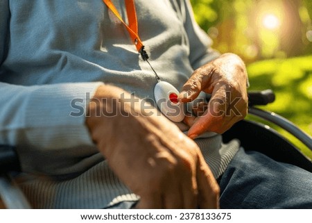 Senior man pressing Alarm Button in a wheelchair outside in a park, closeup. Emergency call system concept image. 