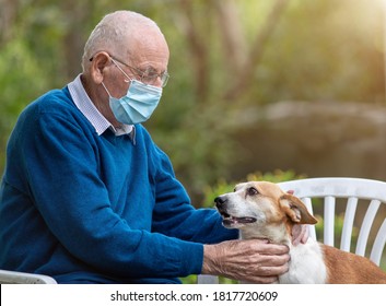 Senior Man With Protective Mask Cuddling Cute Dog In Garden With Green Background