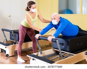 Senior Man In Protective Mask Workout In Rehabilitation Center. Personal Trainer Helping Senior Man