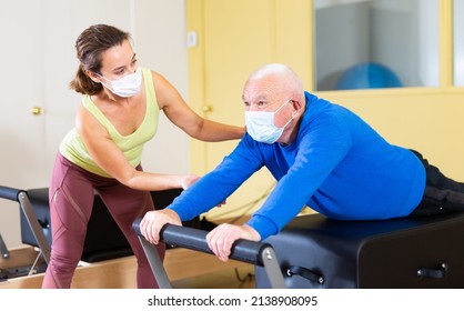 Senior Man In Protective Mask Workout In Rehabilitation Center. Personal Trainer Helping Senior Man