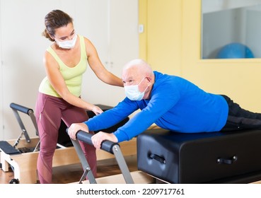 Senior Man In Protective Mask Workout In Rehabilitation Center. Personal Trainer Helping Senior Man