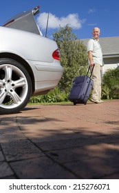 Senior Man Pulling Suitcase On Wheels From Parked Car Boot On Driveway, Smiling, Side View, Portrait (surface Level)