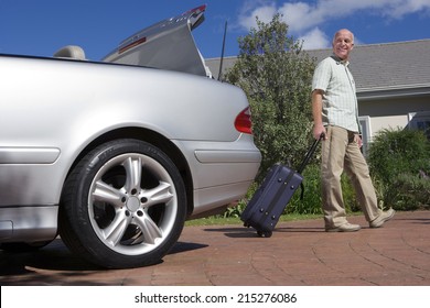 Senior Man Pulling Suitcase On Wheels From Parked Car Boot On Driveway, Smiling, Side View, Portrait (surface Level)