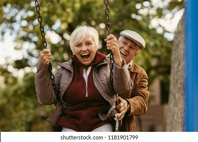 Senior man pushing his female partner on swing in park and having fun together. Playful and happy senior couple enjoying at swing in park . - Powered by Shutterstock