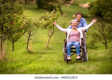 Senior Man Pushing Woman In Wheelchair, Green Autumn Nature