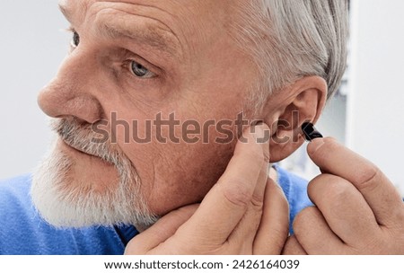 Senior man putting a hearing aid on his ear while visit his doctor at hearing clinic. Hearing solutions for elderly deafness people