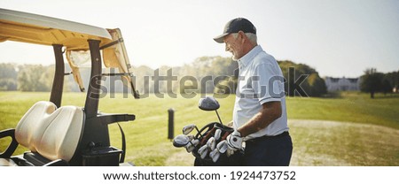Senior man putting his bag full of clubs on a cart while enjoying a round of golf on a sunny day