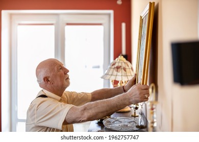 Senior Man Putting Up A Painting On The Wall At His Home
