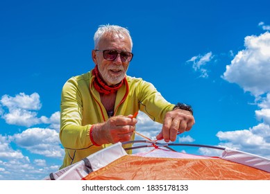 Senior man putting up a tent in the nature with beautiful landscape in the background - Powered by Shutterstock