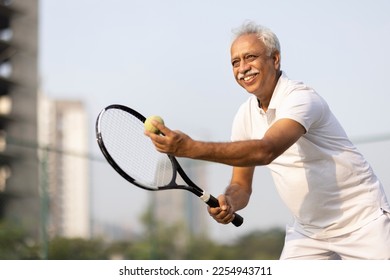 Senior man with racket and ball on tennis court. - Powered by Shutterstock