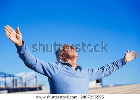 Senior man raising hands sunbathing and closing the eyes enjoying the sun