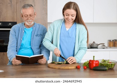 Senior man reading book with nurse cooking in kitchen - Powered by Shutterstock