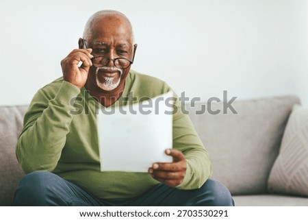 Senior Man Reading a Document While Sitting on a Couch in a Bright Living Room