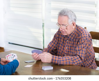 Senior Man With Reading Glasses Thinking About Next Step In Card Game