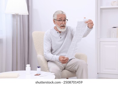 Senior man reading medicine instruction in armchair at home - Powered by Shutterstock