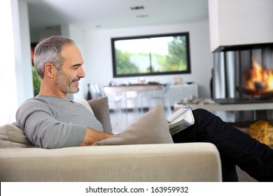 Senior Man Reading Newspaper By Fireplace