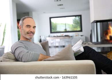 Senior Man Reading Newspaper By Fireplace