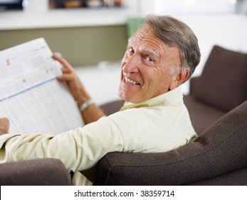 Senior Man Reading Newspaper At Home And Looking Over Shoulders