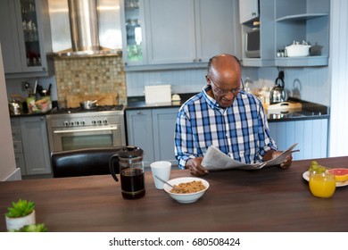 Senior man reading newspaper while having breakfast at table in kitchen - Shutterstock ID 680508424