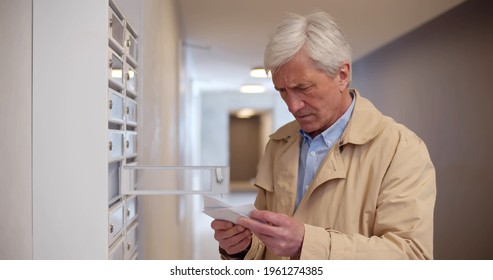 Senior Man Receiving Refusal Letter While Checking Mailbox In Lobby. Portrait Of Aged Tenant Of Apartment House Opening Letterbox In Lobby Receiving Bad News And Feeling Disappointed