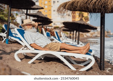 Senior man relaxing on a beach lounger under a straw umbrella by - Powered by Shutterstock