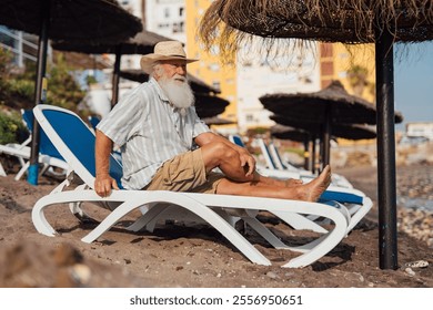 Senior man relaxing on a beach lounger under a straw umbrella by - Powered by Shutterstock