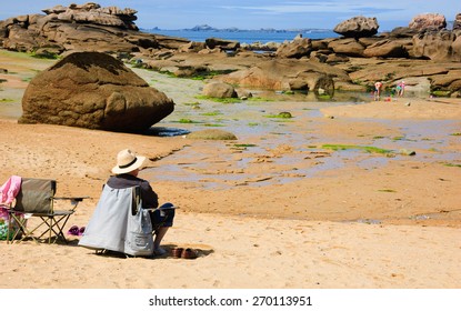 Senior man relaxing at Pink Granite Coast (Brittany, France) and looking at his grandchildren playing. Family summer vacation background. - Powered by Shutterstock