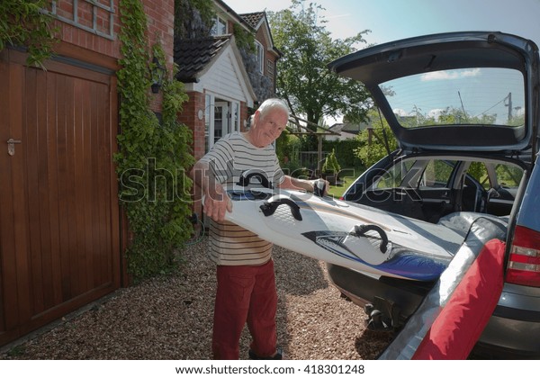 Senior man removing\
surfboard from car boot