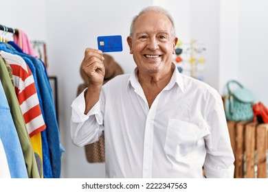 Senior man at retail shop holding credit card looking positive and happy standing and smiling with a confident smile showing teeth  - Powered by Shutterstock