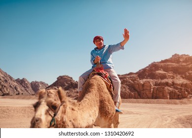 Senior man rides a camel in desert by Sinai mountains. Happy tourist waving at camera - Powered by Shutterstock