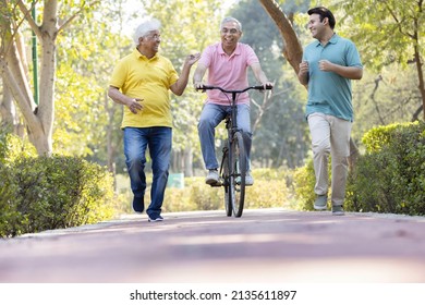 Senior Man Riding Bicycle With Other Old Man And Son Running While Having Fun At Park
