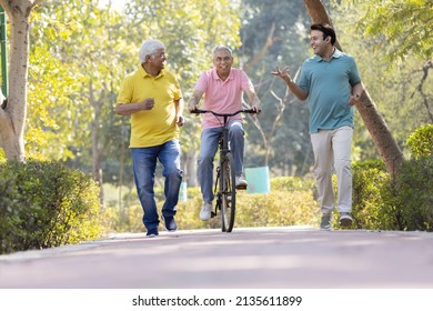 Senior Man Riding Bicycle With Other Old Man And Son Running While Having Fun At Park
