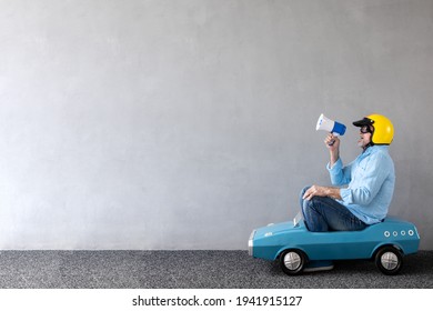 Senior man riding toy car. Full length portrait of funny businessman against concrete wall with copy space. Business start up concept