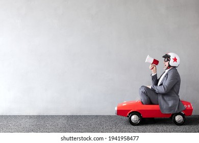 Senior man riding toy car. Full length portrait of funny businessman against concrete wall with copy space. Business start up concept - Shutterstock ID 1941958477