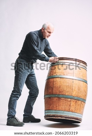 Senior man rolling a barrel of wine in front of him on edge in a full length isolated view on white in a viticulture or wine production concept
