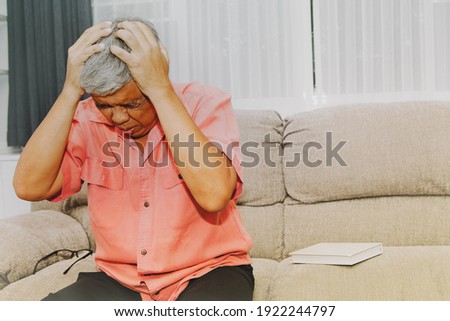 Senior man sat on the couch at home, getting dizzy and headaches during too long reading, causing stress.