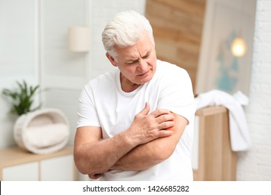 Senior Man Scratching Arm Indoors. Allergy Symptom