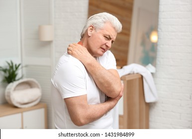 Senior man scratching neck indoors. Allergy symptom