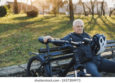 A senior man is seated on a bench next to a bicycle. He appears relaxed, looking around the area. - Powered by Shutterstock