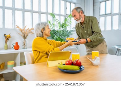 Senior man serving breakfast to share with his wife while she is using digital tablet sitting on the living room - Powered by Shutterstock