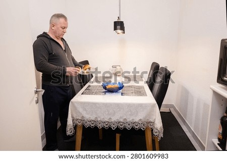 Senior man setting the table at home. Household chores in older age, active retirement, shared domestic responsibilities and gender equality in everyday life.