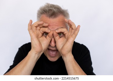 Senior Man Shaping Glasses With Fingers. Male Model In Black T-shirt Making Gesture Forming Goggles With Both Hands, Having Fun. Portrait, Studio Shot, Making Funny Face Concept.