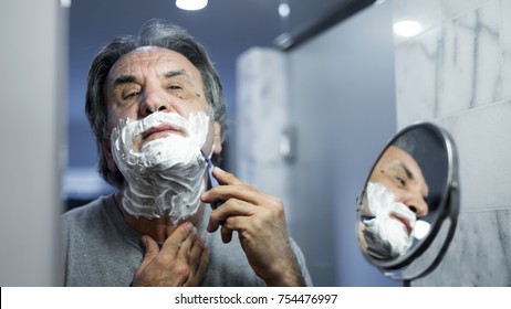 Senior man shaving his beard in bathroom - Powered by Shutterstock