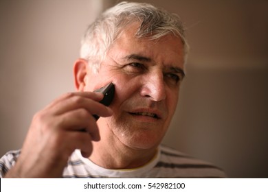 Senior Man Shaving At Home, Using Electric Razor. Space For Copy. 