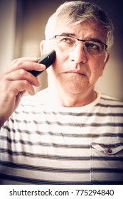 Senior Man Shaving At Home, Using Electric Razor.