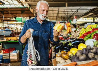 Senior man shopping at the farmer's market. One elderly man buying a fresh vegetable at a community marketplace. - Powered by Shutterstock