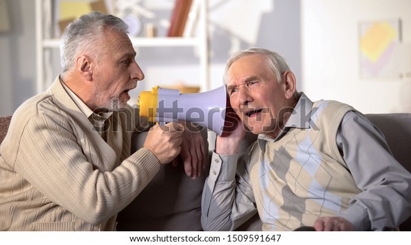 Senior man shouting bullhorn to deaf friend,\
old aged health, deafness\
treatment