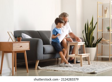 Senior Man Showing His Little Grandson How To Make Paper Boat At Home