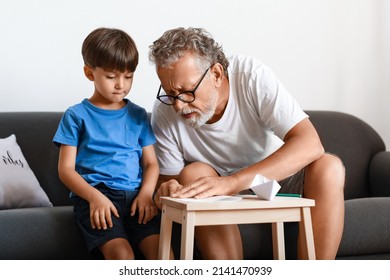 Senior Man Showing His Little Grandson How To Make Paper Boat At Home