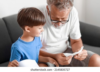 Senior Man Showing His Little Grandson How To Make Paper Boat At Home